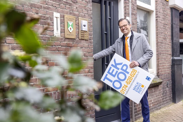 Makelaar met Te Koop-bord bij een woning